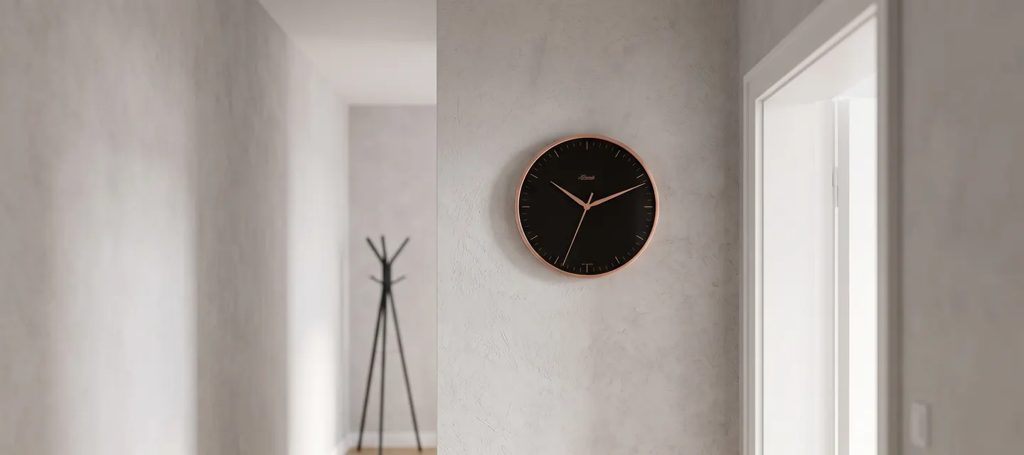 Horloge murale industrielle à cadran vitré et contour métallique brillant installée dans un couloir minimaliste.